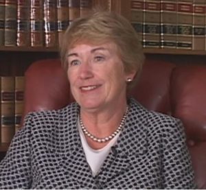 Elizabeth Bermingham Lacy is seated in a chair in front of a bookcase during the October 2008 interview. She is wearing a printed blazer and pearl jewelry. 