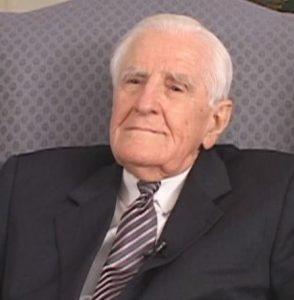 Harry L. Carrico seated in a chair wearing a suit and tie.