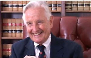 Charles S. Russell speaking during the 2007 interview. He is seated in a chair in front of a book shelf wearing a suit and tie.