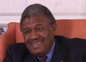 John Charles Thomas speaking during the June 2007 interview. He is seated in a chair wearing a suit and tie.