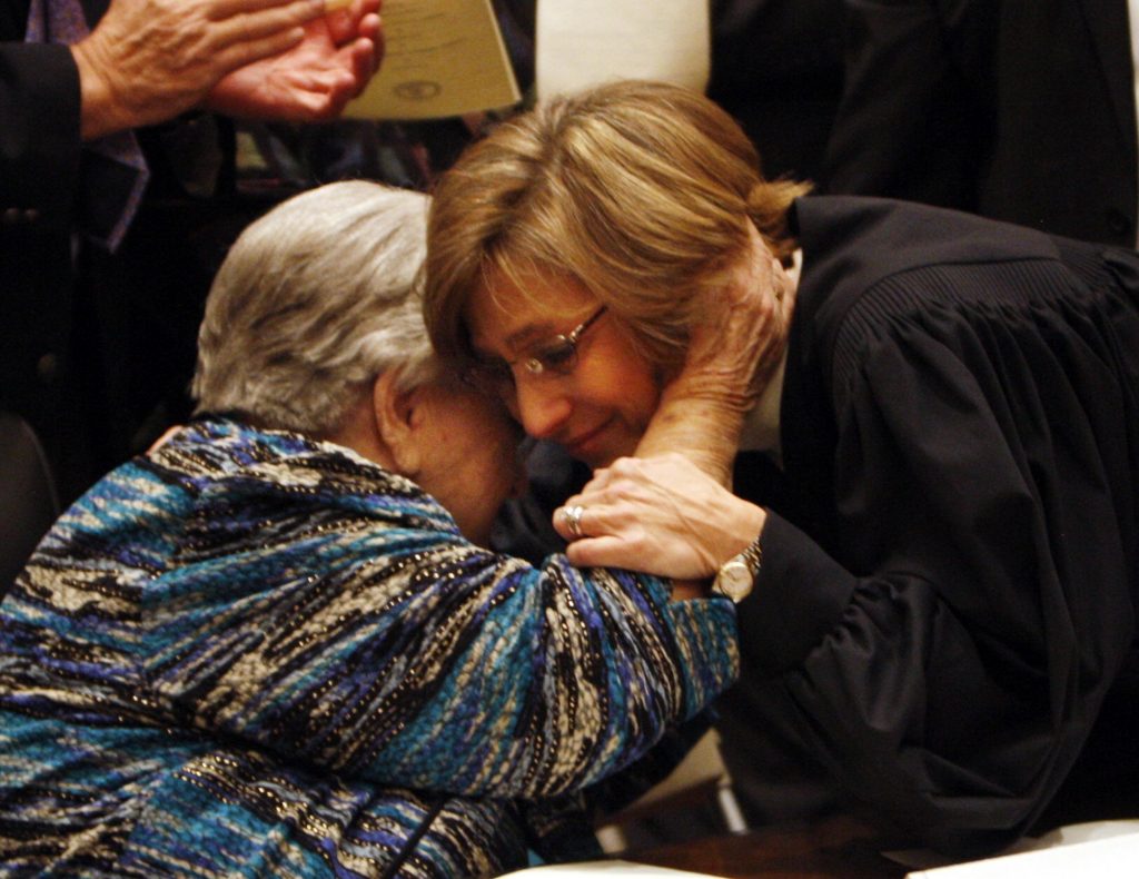 Chief Justice Cynthia Dinah Fannon Kinser hugs her mother, Mrs. Velda M. Fanno. Chief Justice Kinser wears a judicial robe and her mother wears a blue, purple, black and tan printed blouse. 