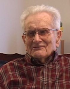 Allen L. Lucy speaking during the 2009 interview. He is seated in a chair wearing a plaid button down shirt. 