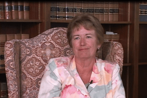 Elizabeth Bermingham Lacy is seated in a chair in front of a book shelf during the September 2008 interview. She is wearing a floral blouse.
